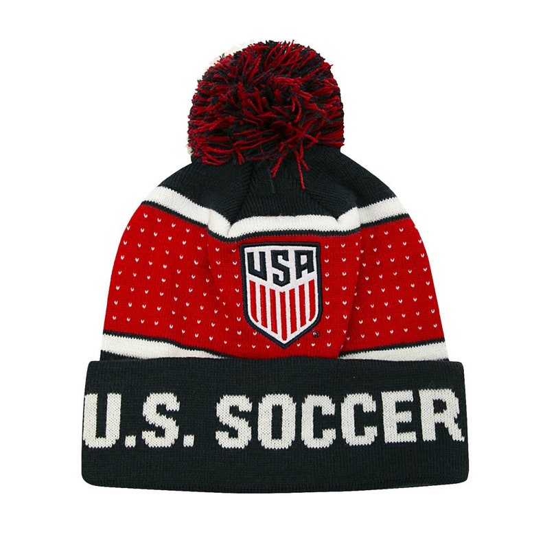 May include: A navy blue and red knit beanie with a white pom pom and a white "U.S. SOCCER" logo. The beanie also features a red and white USA crest.