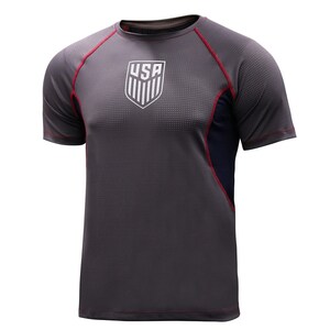 May include: Gray athletic t-shirt with the USA emblem on the chest. The shirt has red trim along the sleeves and shoulders, and a navy blue panel on the side. The fabric has a textured, dotted pattern.