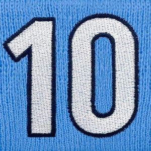 May include: A close-up shot of the number 10 embroidered onto a light blue knitted fabric. The number is white with a navy blue border, displaying a textured, stitched design. The fabric has a knitted appearance.