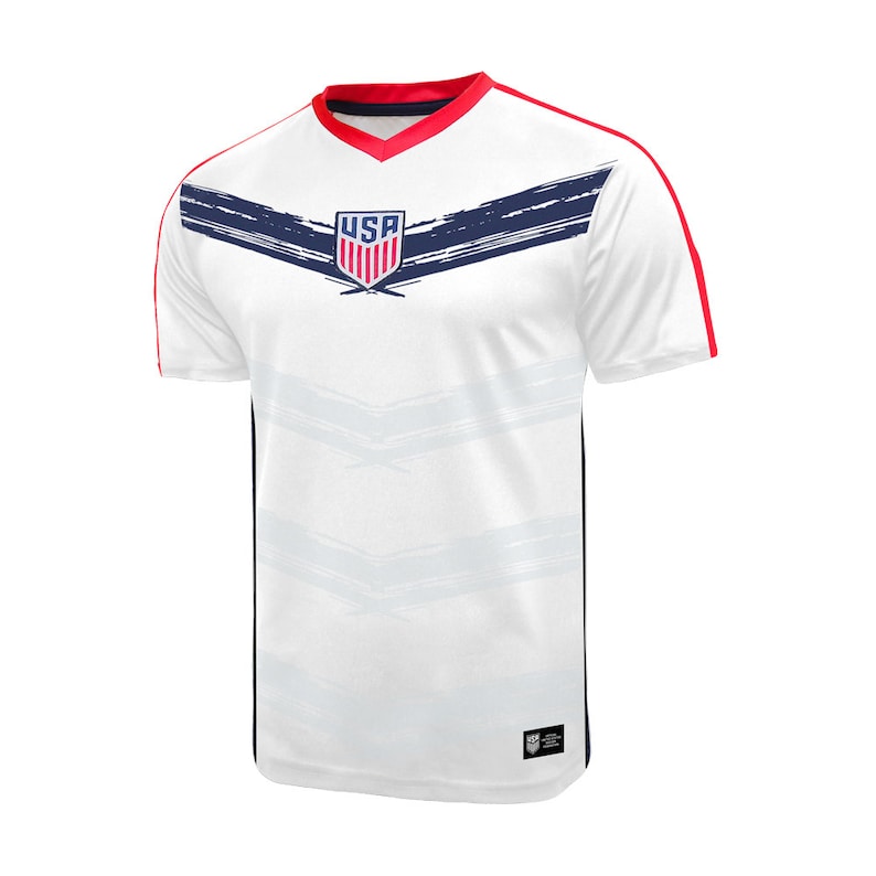 May include: White soccer jersey with red and blue trim. The jersey has a blue and white USA logo on the front with a brushstroke design.