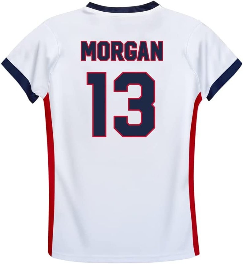 May include: White soccer jersey with red and blue trim. The back of the jersey has the name "MORGAN" and the number "13" in navy blue with a red outline.