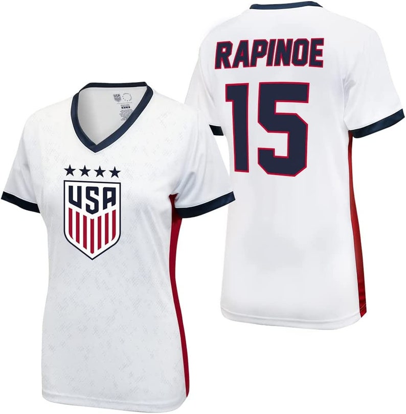 May include: White soccer jersey with red and navy blue accents. The jersey has the USA crest on the front and the name "RAPINOE" and the number "15" on the back.