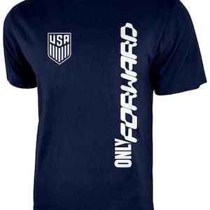 May include: A navy blue t-shirt with a white graphic of the USA soccer team logo and the text "ONLY FORWARD" on the right side.