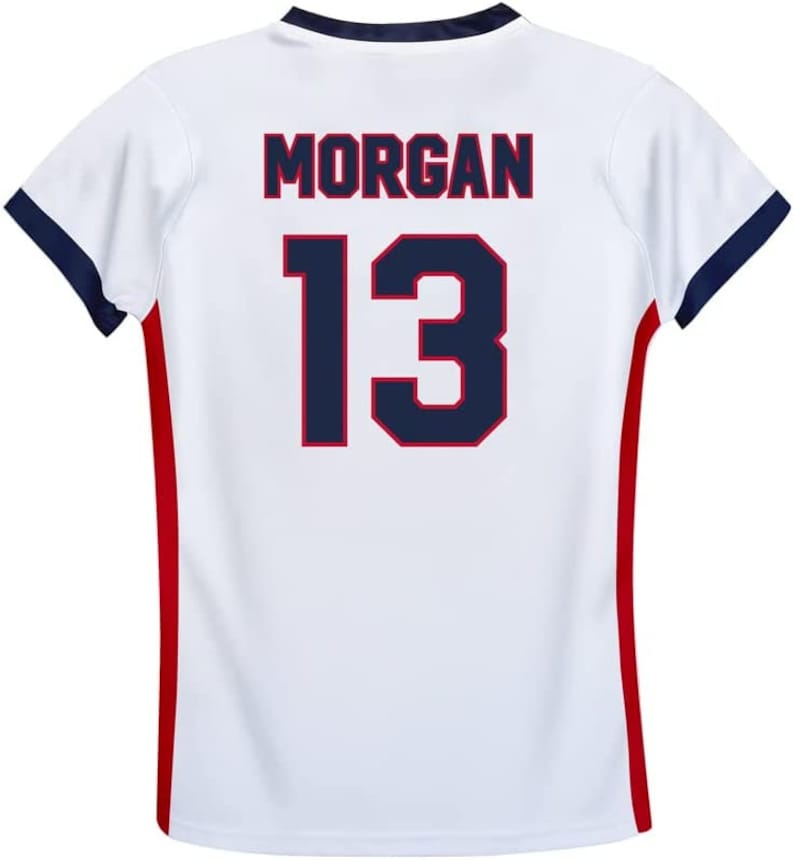 May include: White soccer jersey with red and blue trim. The back of the jersey has the name "MORGAN" and the number "13" in navy blue with a red outline.