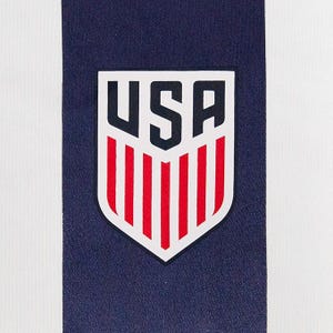 May include: Close-up of a white and navy blue fabric with a vertical stripe design. The navy blue stripe features a USA emblem with red vertical stripes and white borders. The emblem is centered on the fabric.