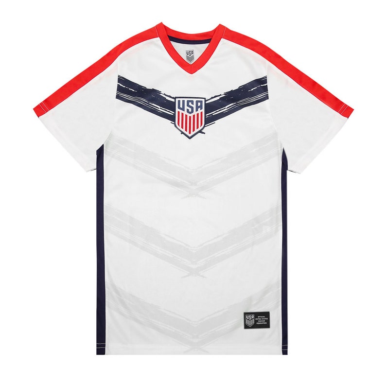 May include: White soccer jersey with red and navy blue accents. The jersey features a stylized brushstroke design and the word "USA" in a navy blue shield.