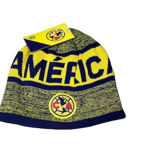 May include: Yellow and blue knitted beanie with the word "AMERICA" in navy blue lettering and a blue and yellow logo with the letters "CA" in the centre.