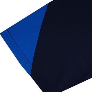 May include: Close-up of a navy blue and royal blue athletic shirt. The shirt features a color block design with a royal blue shoulder and sleeve panel. The seams are visible, and the fabric appears to be a smooth, athletic material.