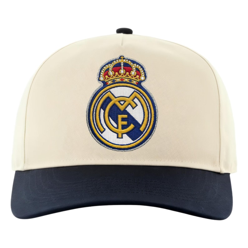 May include: Cream-colored baseball cap with a navy blue brim and a black button. The cap features an embroidered emblem with a crown and the letters "MCF" in gold, blue, and white. A stylish accessory for sports fans.