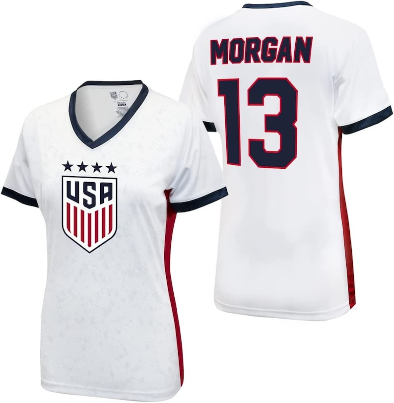 Puede incluir: Camiseta de f&uacute;tbol blanca con ribetes rojos y azul marino. La camiseta tiene el logotipo de EE. UU. en la parte delantera y el nombre "MORGAN" y el n&uacute;mero "13" en la parte posterior.