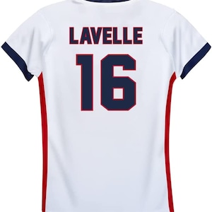 Op de afbeelding: Wit voetbaltenue met rode en blauwe bies. De achterkant van het tenue heeft de naam "LAVELLE" en het nummer "16" in donkerblauw met een rode omlijsting.