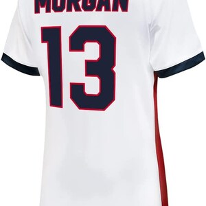 Puede incluir: Camiseta de f&uacute;tbol blanca con ribetes rojos y azules. La parte posterior de la camiseta tiene el nombre "MORGAN" y el n&uacute;mero "13" en azul marino con un contorno rojo.