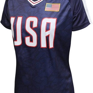 May include: Navy blue athletic shirt with the word "USA" in large white letters outlined in red. The shirt has a V-neck collar with red and white trim, white stripes on the sleeves, and an American flag patch.