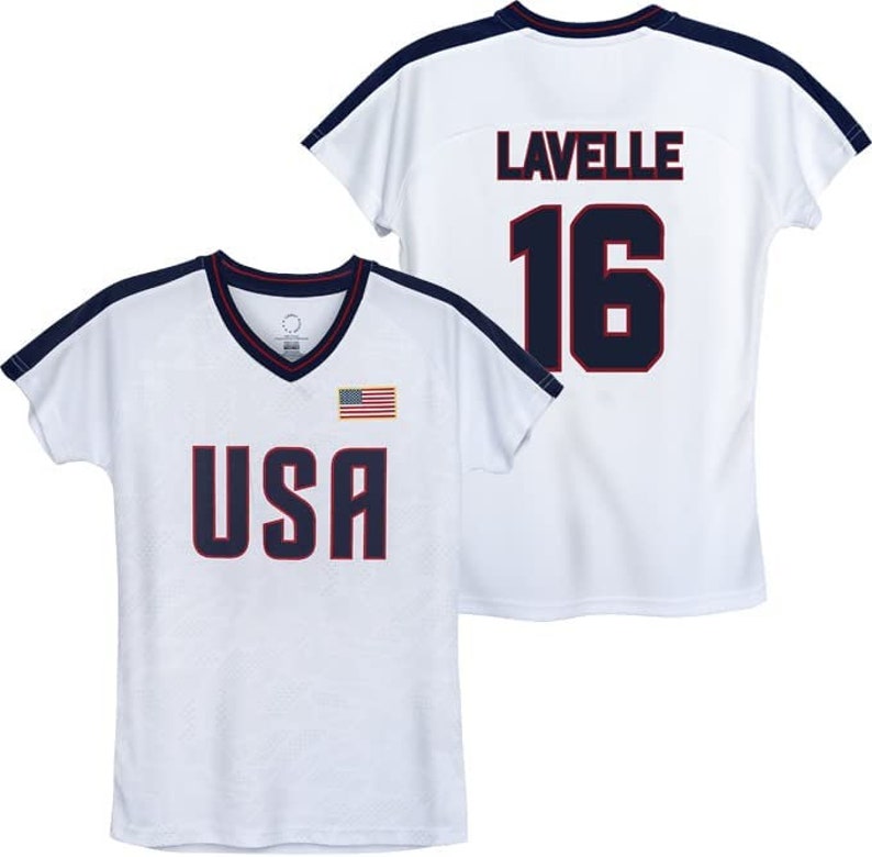 Puede incluir: Camiseta blanca con ribete azul marino y las palabras "USA" y una peque&ntilde;a bandera estadounidense en la parte delantera. La parte posterior de la camiseta tiene el nombre "Lavelle" y el n&uacute;mero "16" en azul marino.