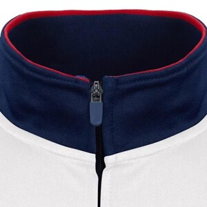 Puede incluir: Una chaqueta blanca con cremallera, con un cuello azul marino y ribete rojo. El cuello est&aacute; forrado con tela roja.