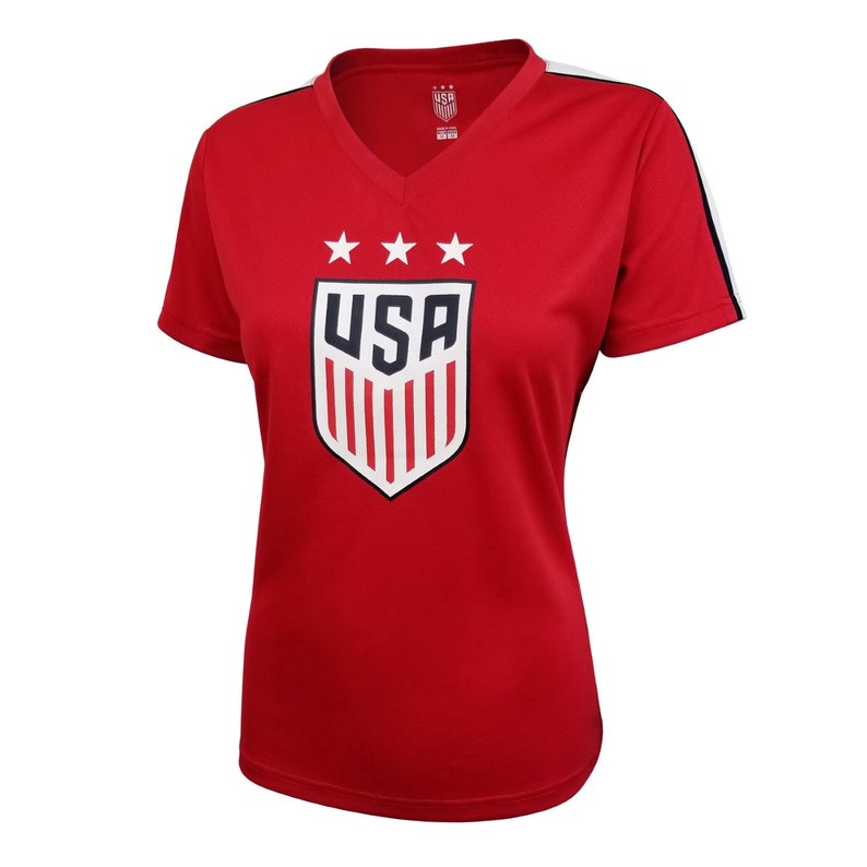 Pode incluir: Camiseta vermelha de manga curta com um bras&atilde;o dos EUA branco e azul com cinco estrelas e a palavra "USA". A camiseta tem listras brancas e pretas nos ombros.