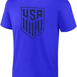 May include: A royal blue t-shirt with a distressed navy blue graphic of the USA shield logo.