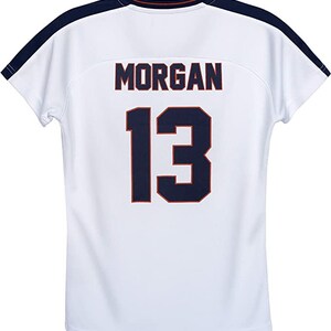 May include: White soccer jersey with navy blue and red trim. The back of the jersey has the name "MORGAN" and the number "13" printed in navy blue.