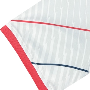 May include: Close-up of a white athletic shirt with a pattern of vertical grey stripes and lightning bolt shapes. The shirt has red trim on the sleeve and a red stripe across the chest. A thin navy blue stripe is also visible.