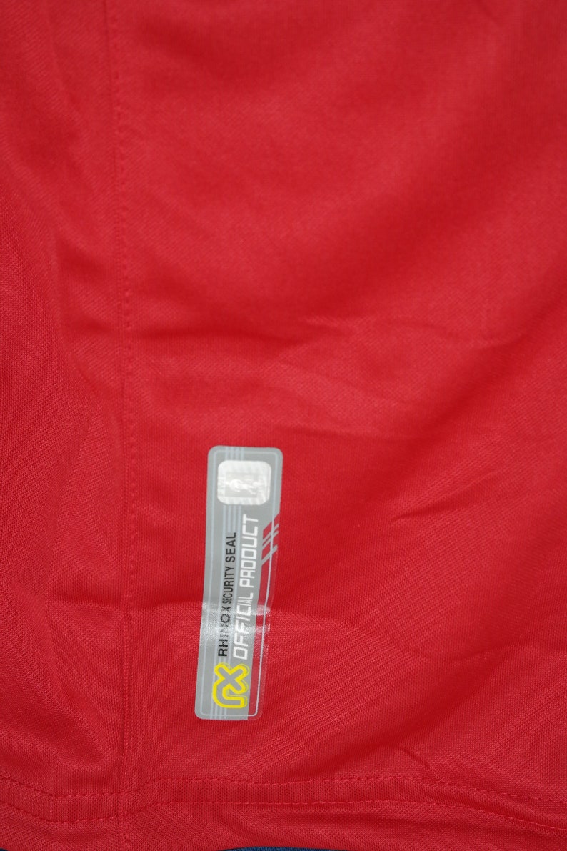 May include: A red shirt with a gray and white security seal tag that reads "Official Product" and "Rhino X Security Seal".