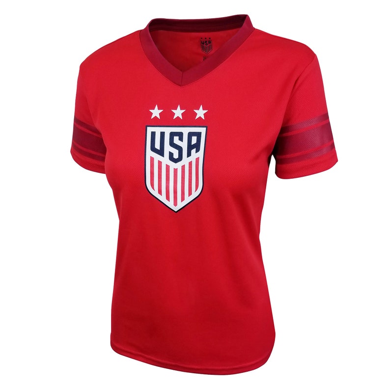 K&ouml;nnte beinhalten: Rotes Kurzarm-Trikot mit einem wei&szlig;en und blauen USA-Wappen und drei Sternen &uuml;ber dem Wappen. Das Trikot hat rote und wei&szlig;e Streifen an den &Auml;rmeln.