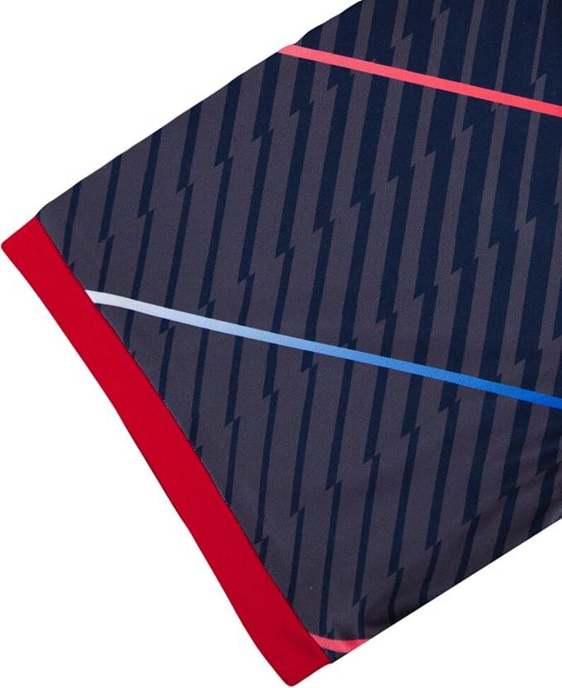 May include: A section of a navy blue garment with a repeating pattern of gray lightning bolts. The edge is trimmed with a vibrant red border. Thin lines of red, white, and blue cross the fabric diagonally.