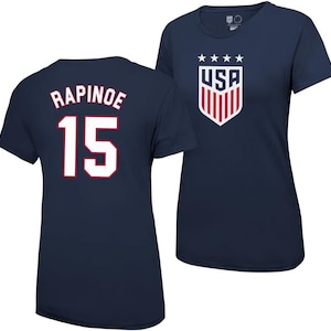 Pode incluir: Duas camisas azul-marinho. Uma tem o n&uacute;mero "15" e o nome "RAPINOE" impresso nas costas. A outra tem um bras&atilde;o dos EUA vermelho, branco e azul com cinco estrelas acima.