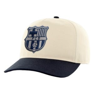 May include: Cream-colored baseball cap with a navy blue brim. The cap features an embroidered crest with the letters "FCB" in navy blue. The cap has a curved brim and a black button on top.