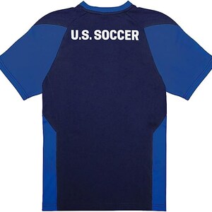 May include: A navy blue and royal blue short-sleeved t-shirt with the text "U.S. SOCCER" printed on the back.