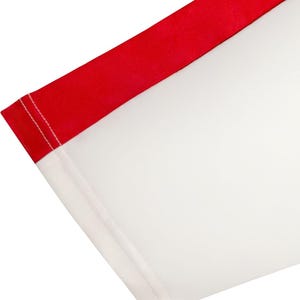 May include: Close-up of a white fabric with a red border. The red border is on the top edge and is a solid color. The white fabric is a large area of the image. The edges are sewn with white thread.