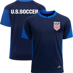 May include: Navy blue soccer jersey with blue accents on the sleeves and collar. The front features a USA crest, and the back displays "U.S. SOCCER" in white block letters. The jersey is made of a lightweight, breathable material.