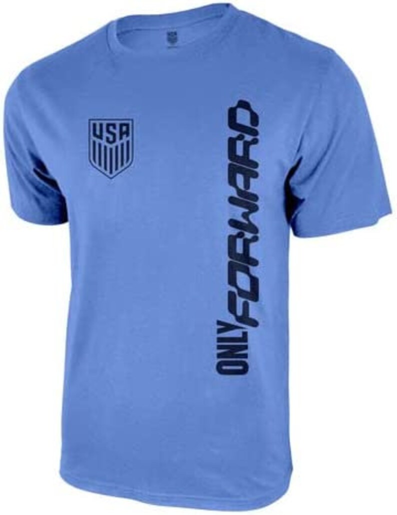 Op de afbeelding: Een lichtblauw t-shirt met een donkerblauwe afbeelding van het USA-logo en de tekst "ONLY FORWARD" die verticaal aan de rechterkant is gedrukt.