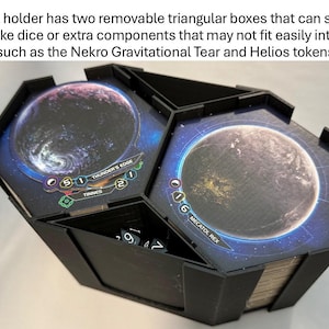 May include: Black hex-shaped game component holder with two removable triangular boxes. The boxes feature planet graphics and text. Dice are visible inside one compartment. Ideal for storing game components.