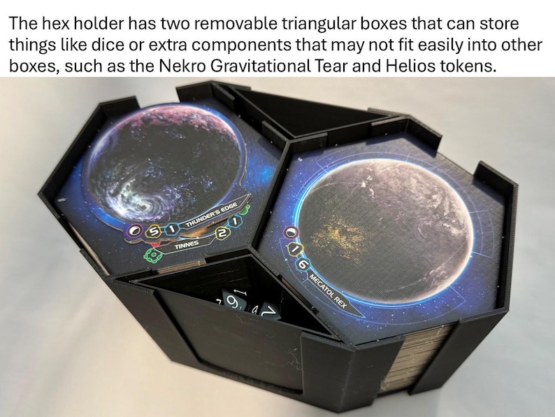 May include: Black hex-shaped game component holder with two removable triangular boxes. The boxes feature planet graphics and text. Dice are visible inside one compartment. Ideal for storing game components.