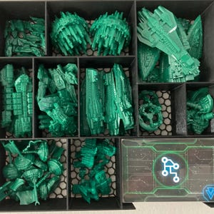 May include: A black organizer filled with various green plastic game pieces, including spaceship models and other futuristic components. A card with a circuit board design is visible in the bottom right corner.