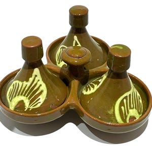 May include: A set of three olive green ceramic tajines connected by a central handle. Each conical lid features a hand-painted cream-colored abstract pattern. The glazed finish is smooth and reflective, with a consistent earthy tone throughout the piece.