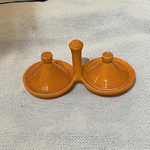 May include: Orange ceramic condiment server with two lidded compartments and a central handle. The lids and base have a glossy finish with a white trim. The server is designed for serving sauces or spices.