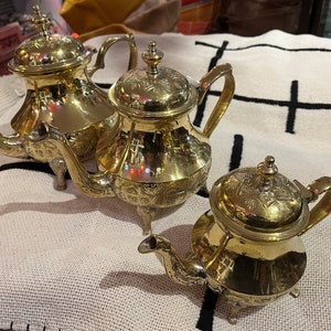 May include: Three ornate gold teapots with intricate designs and a polished finish. The teapots have a traditional style and are perfect for serving tea.