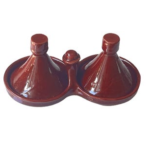 May include: A double-chambered brown glazed ceramic tajine serving dish featuring two conical lids and a central handle. The glossy finish covers the entire exterior of the connected circular bases and the pointed tops of the lids.