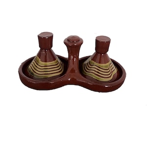 May include: A brown ceramic condiment set featuring two conical tajine-style lids with horizontal beige and brown striped patterns. The two circular bases are connected by a central handle with a rounded top, all finished in a glossy glaze.