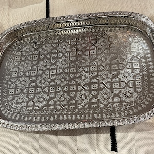Peut inclure: Un plateau de service ovale en argent avec un motif en relief complexe. Le plateau a un bord surélevé et une bordure décorative.