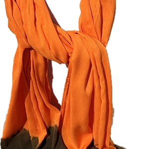 May include: A long, orange and brown ombre scarf. The scarf is made of a soft, lightweight fabric and has a fringed edge.