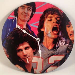 May include: A round clock with a black background and a colorful image of four musicians. The clock has white hands and a white center. The musicians are wearing colorful clothing and have their hair styled in the 1970s.