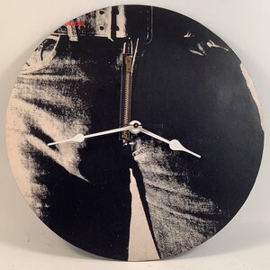 May include: A black and white clock with a zipper detail. The clock face is a close-up of a pair of jeans.