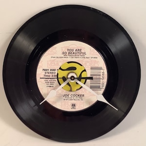 May include: A black vinyl record with a yellow and black label. The label has the text "You Are So Beautiful" by Joe Cocker. The record is a 45 RPM single and has a clock face on it.
