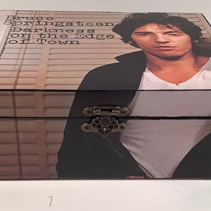 May include: A wooden box with a hinged lid and a metal clasp. The box is decorated with a photo of Bruce Springsteen and the album title "Darkness on the Edge of Town".