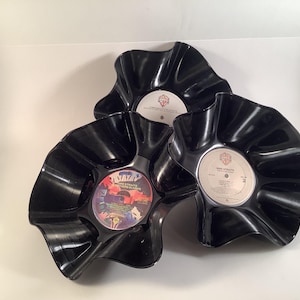 May include: Three black vinyl record bowls with ruffled edges. The bowls are decorated with album covers featuring the artists Dire Straits, The Stray Cats, and The Ultimate Collection by The Four Tops.