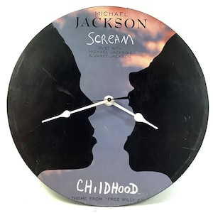 May include: A black vinyl record clock featuring a silhouette of two people with the text "MICHAEL JACKSON SCREAM DUET WITH MICHAEL JACKSON & JANET JACKSON CHIIDHOOD THEME FROM "FREE WILLY 2" printed on it.