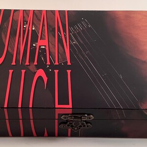 May include: A rectangular box with a black background and the words "HUMAN TOUCH" in red. The box features an image of a musical instrument and a decorative metal clasp.