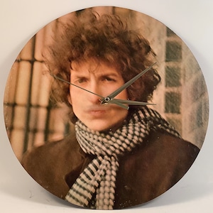 May include: A vintage record clock featuring a close-up image of Bob Dylan. The clock has silver hands and a brown wooden frame.
